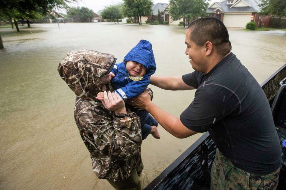 Wilfredo Linares reaches ﻿for his baby, Mason, as they are evacuated from the Grand Mission subdivision﻿ Monday in Fort Bend County﻿. Photo: Brett Coomer, MBO / ' 2017 Houston Chronicle