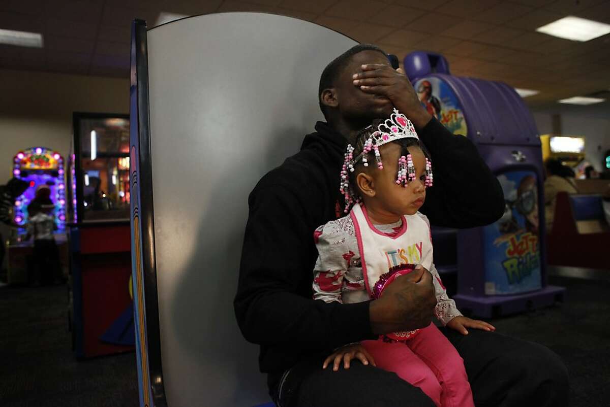 Quindell Anderson covers his eyes with his hand while reading game instructions for the photo booth while holding his daughter LaMya Deshana Price, 1, at Chuck E. Cheese's during her birthday party, Saturday, November 9, 2013, in Hayward, Calif. Photo: Lacy Atkins, The Chronicle